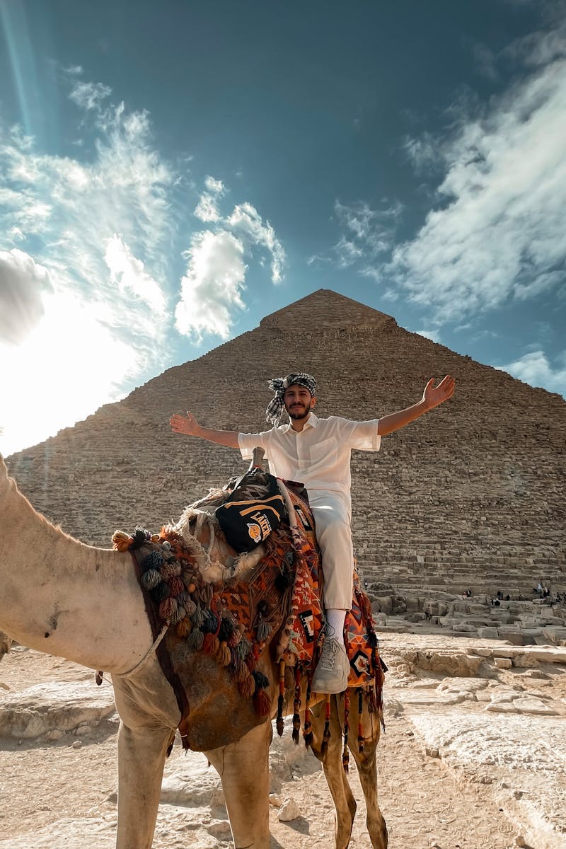 A man sitting on a camel in front of the Giza Pyramid during a stunning sunset, showcasing Egyptian landmarks.